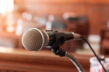 Microphone in Meeting Room A microphone in the foreground and rows of leather seats with wooden trim blurred in the background. It looks like a formal meeting room or court room.