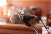 A microphone in the foreground and rows of leather seats with wooden trim blurred in the background. It looks like a formal meeting room or court room. 